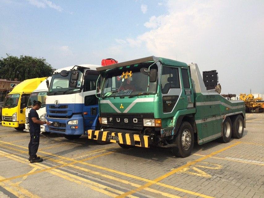 Green Fuso heavy-duty truck parked beside blue and yellow trucks at an industrial lot