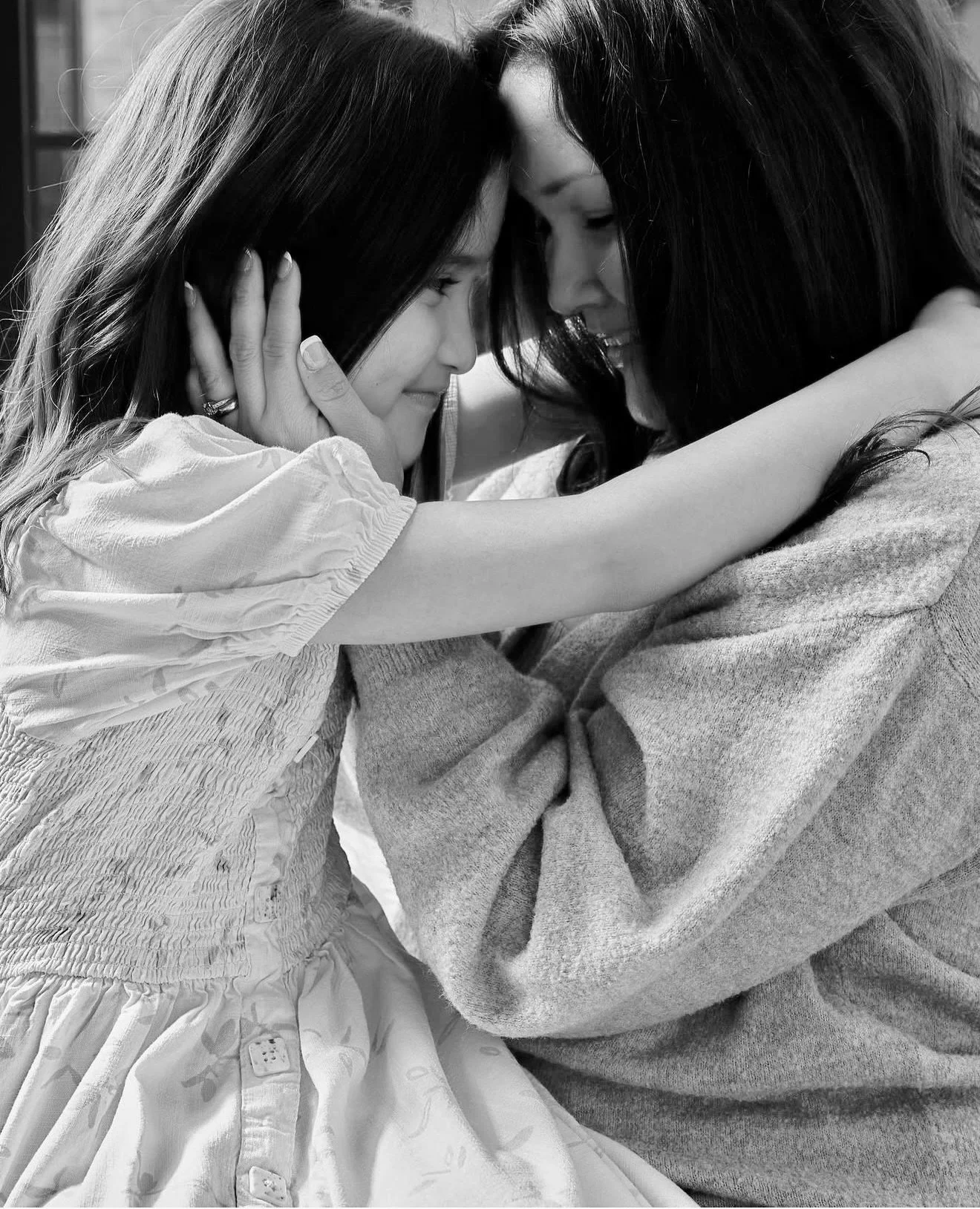 Two women sharing an intimate moment, touching foreheads and smiling, with one gently holding the other's face.