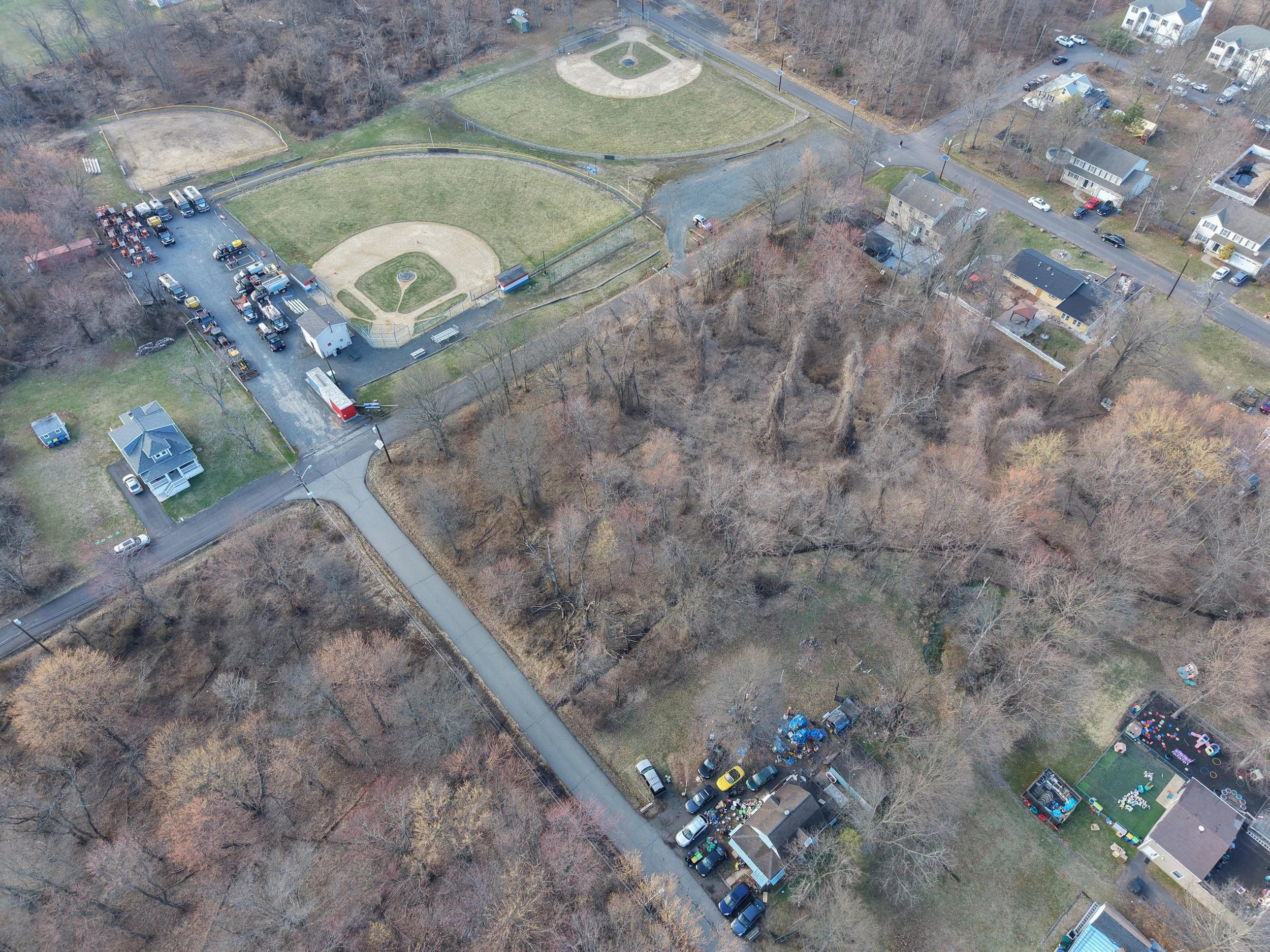 Aerial view of a small neighborhood with playgrounds, parking lots, houses, and trees, some are leafless, during winter.