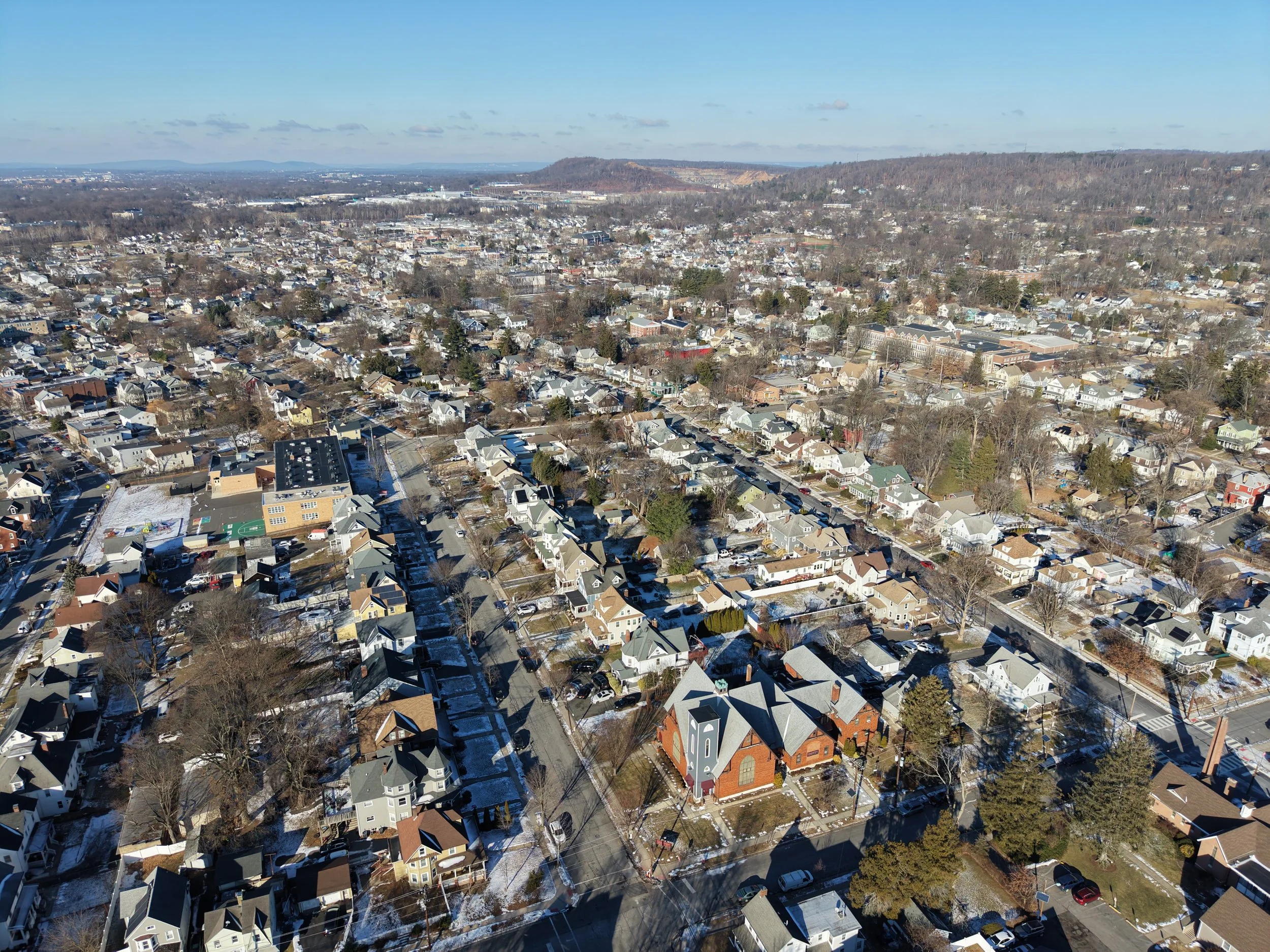 Aerial view of a suburban neighborhood with houses, trees, and streets, with snow on the ground.