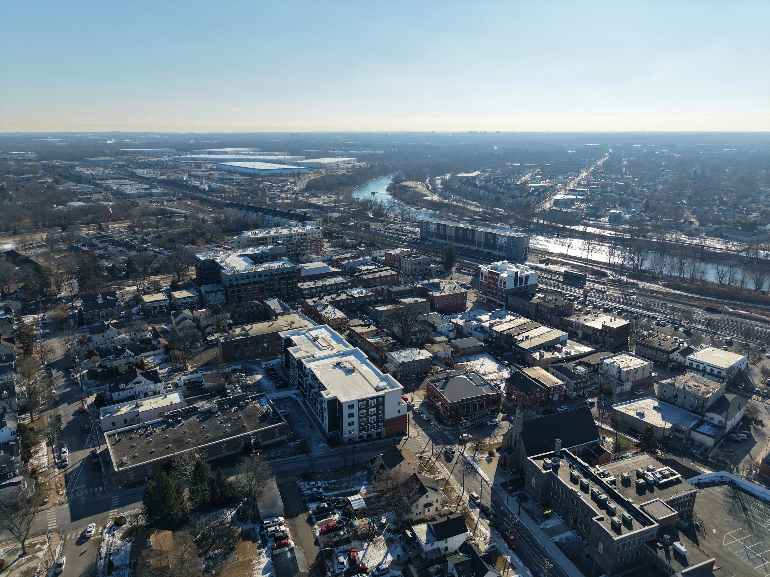 Aerial view of a city with snow-covered buildings and streets, river flowing through the city, and a clear blue sky.