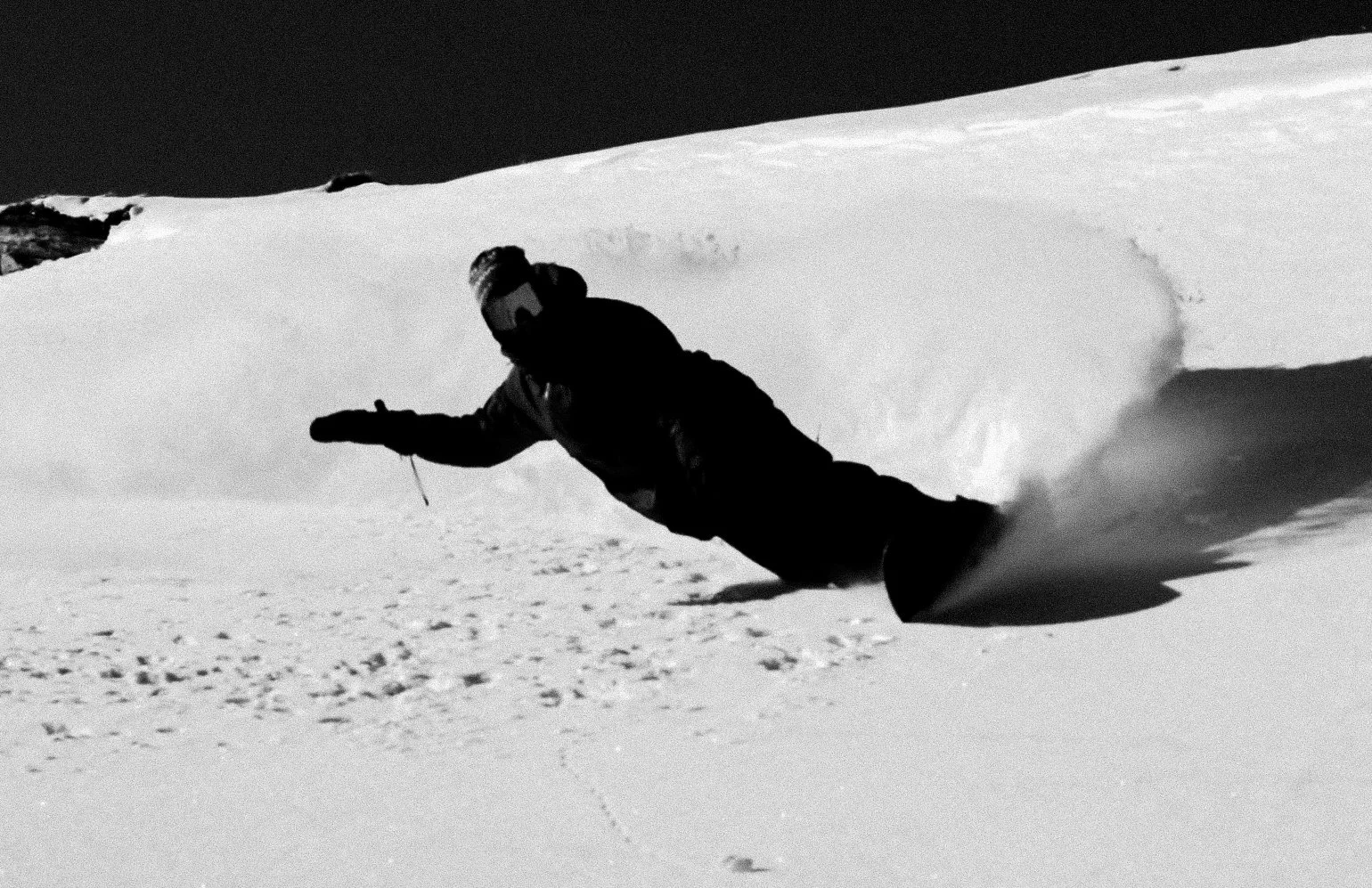 A person wearing winter gear skiing down a snow-covered slope, creating a spray of snow behind them.