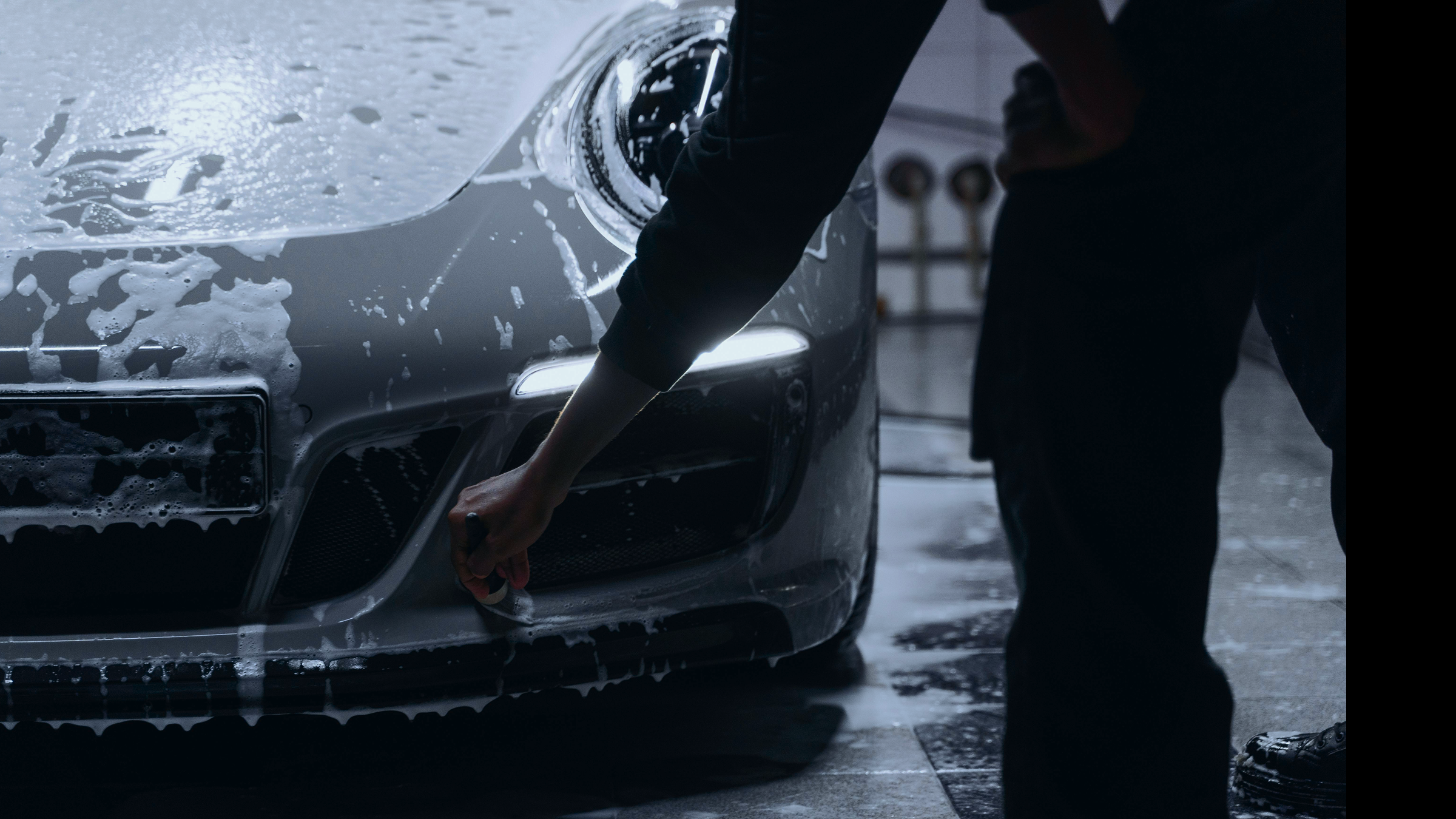 Person washing a silver car with soap at a car wash station.