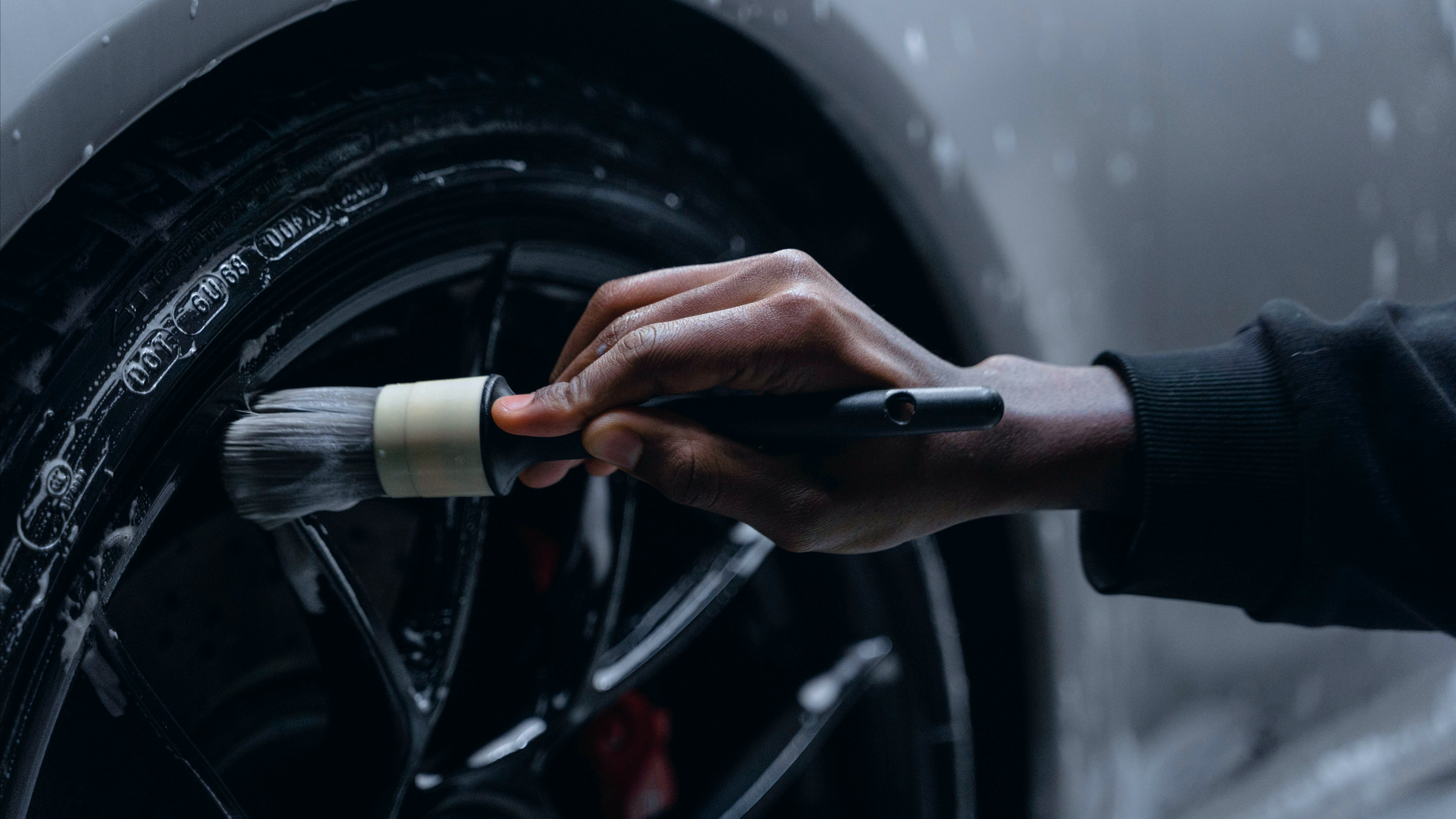 A person cleaning a black car wheel with a brush.
