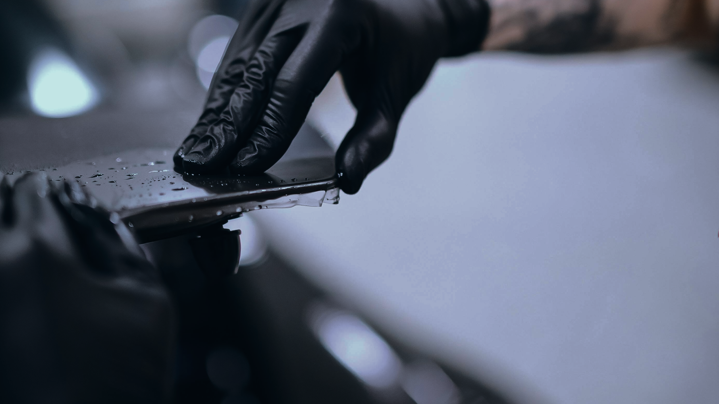 A person wearing black gloves applying a protective film to a car's paint surface.