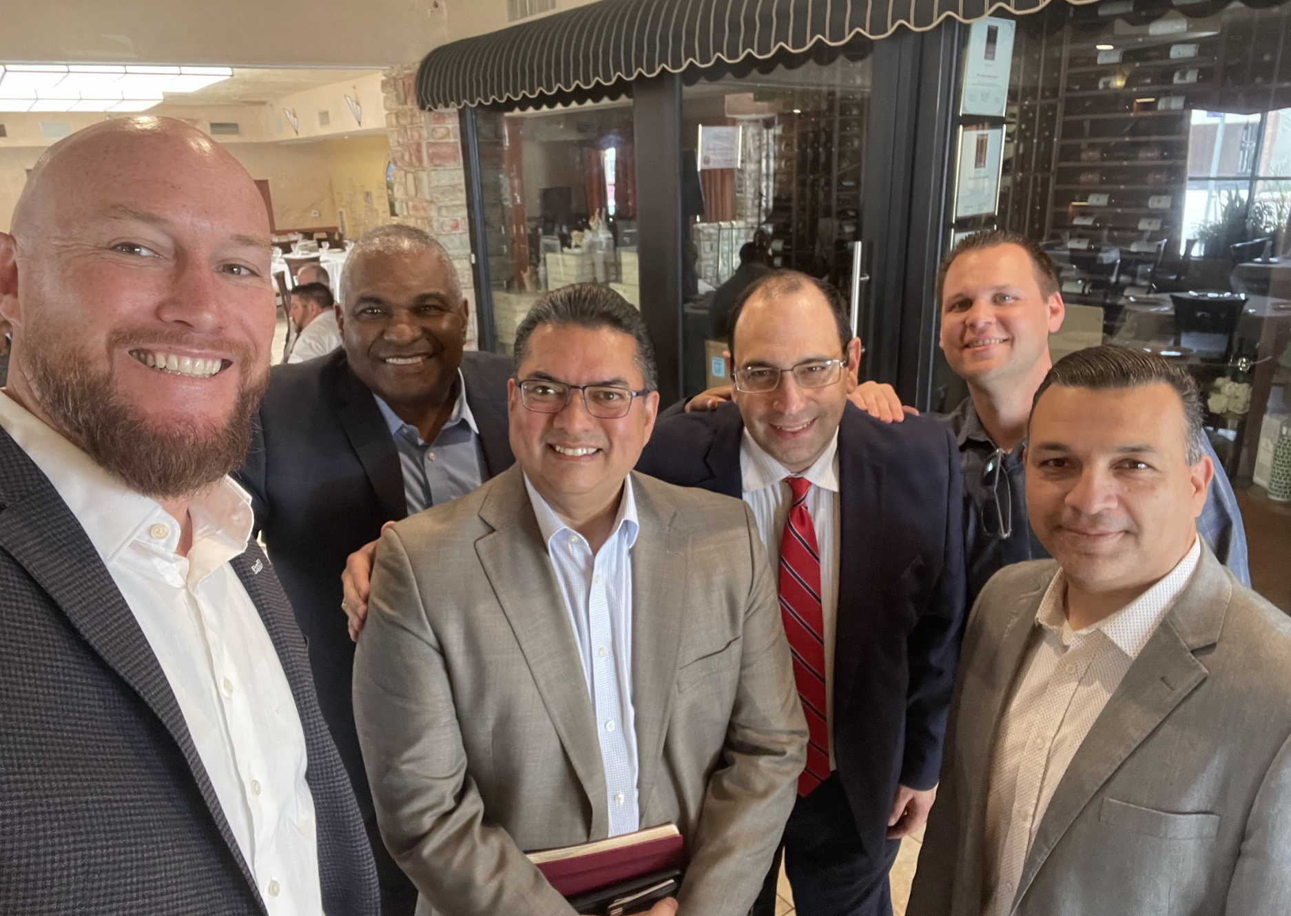 A group of seven men in business attire smiling and posing for a photo inside a restaurant or cafe.