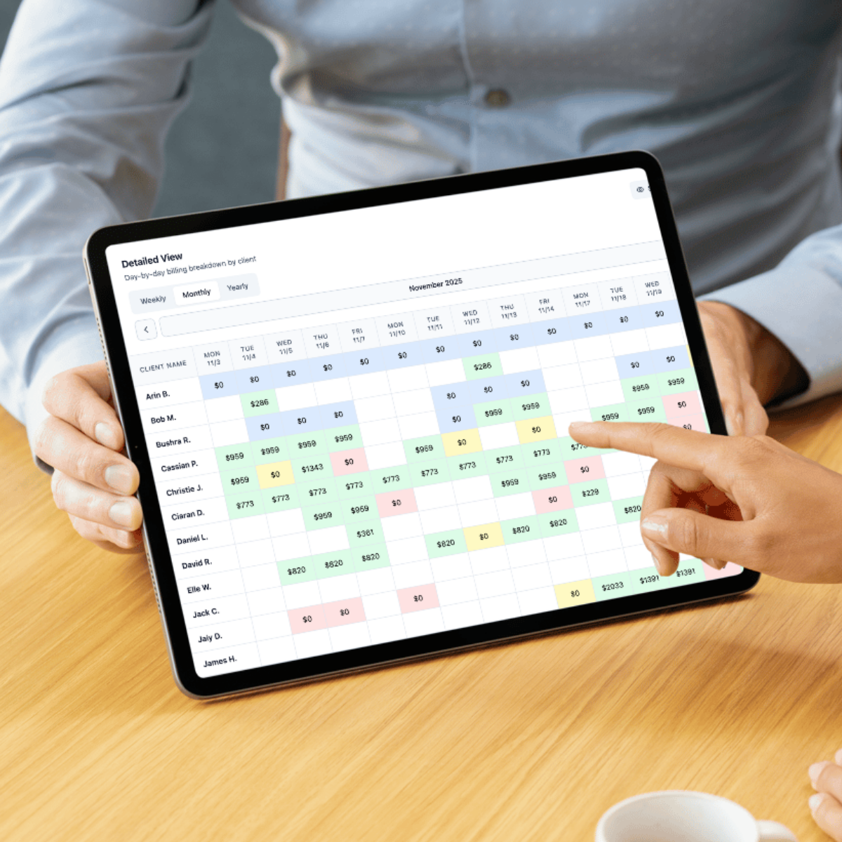 Person pointing at a digital spreadsheet on a tablet, showing a detailed weekly, monthly, and yearly breakdown of client billing for November 2025.