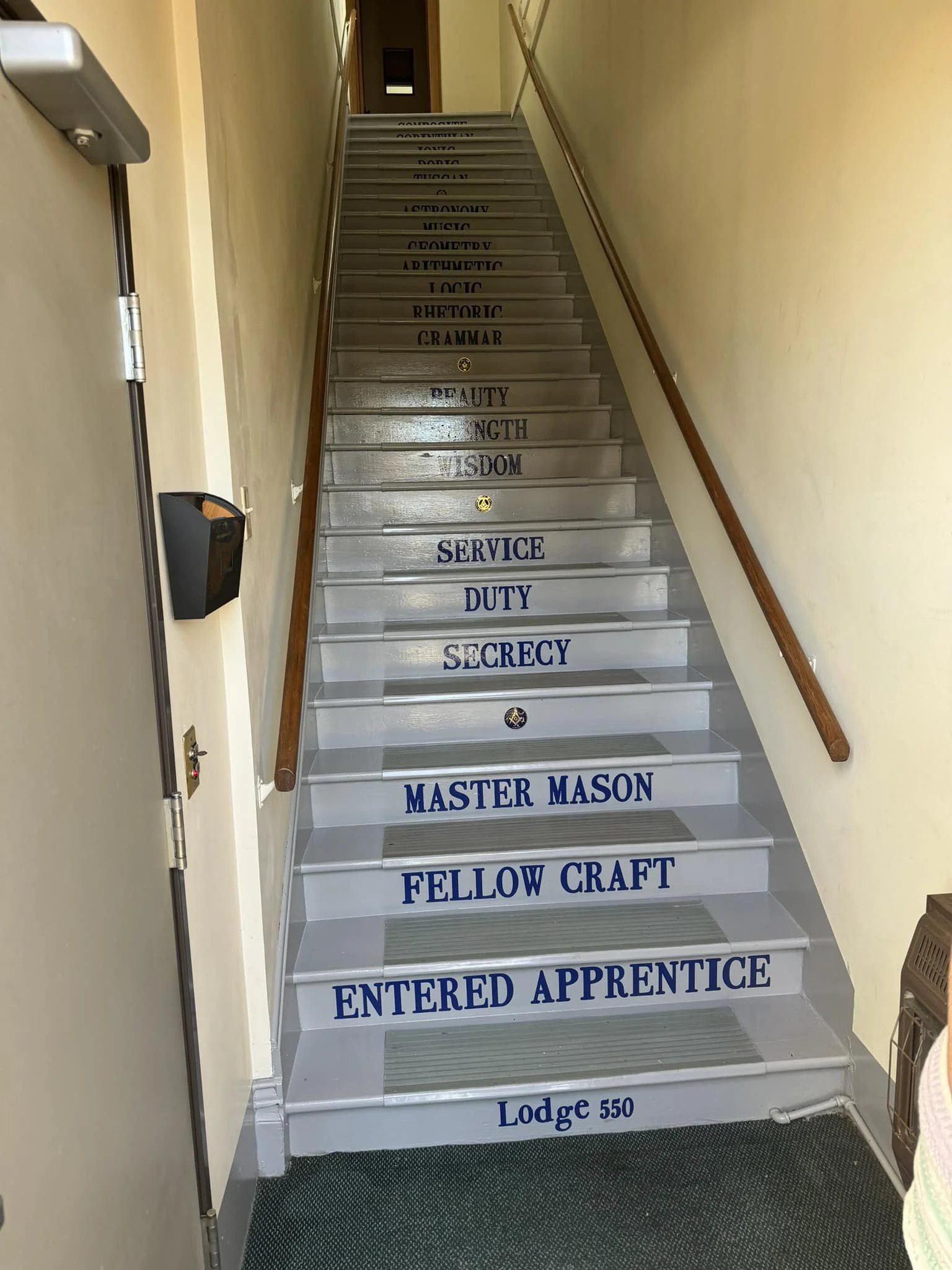 A staircase with spelling words on each step, starting with 'Entered Apprentice' and ending with 'At Lodge 550' at the bottom, inside a building.