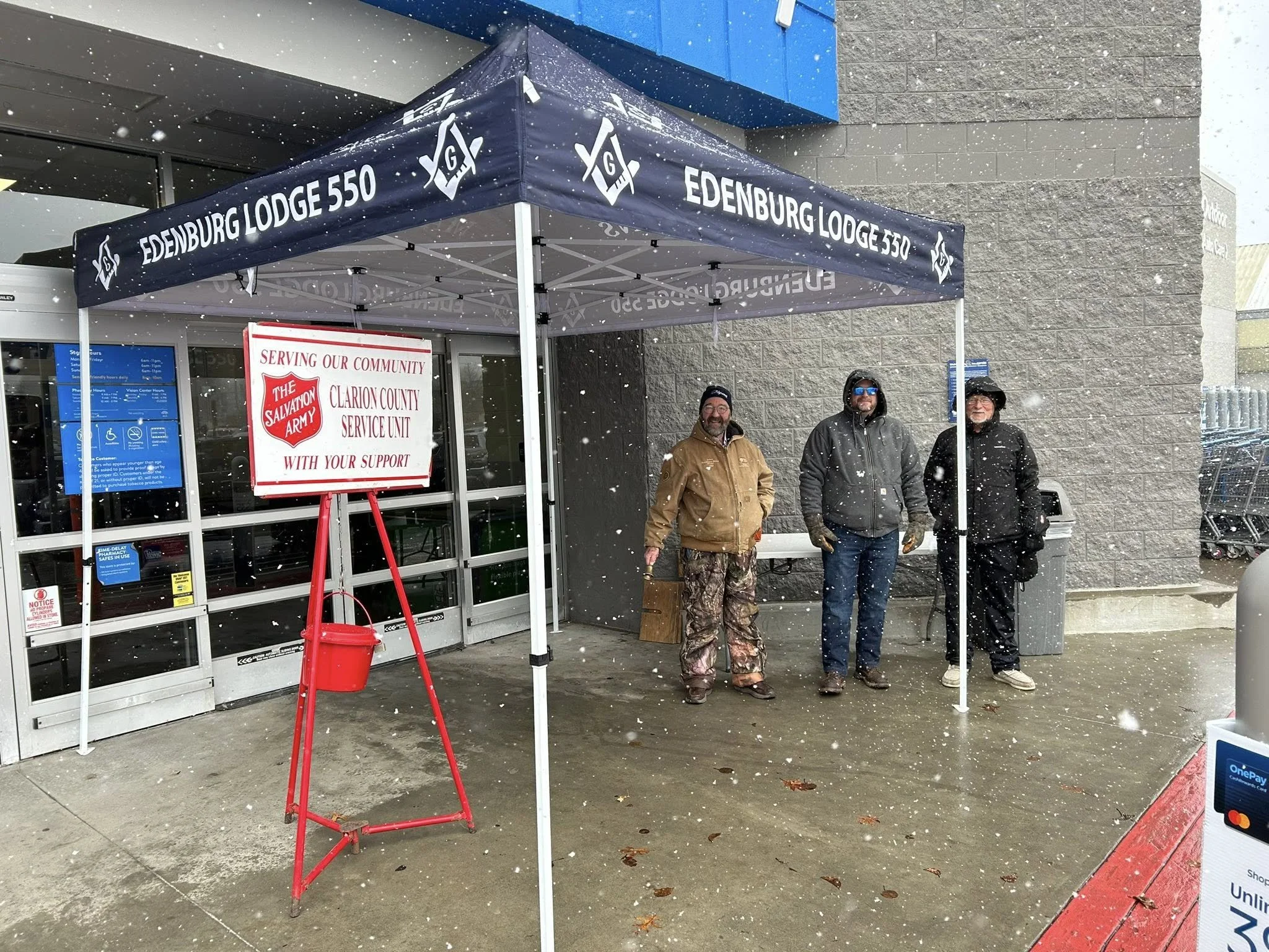 Three men standing outside under a canopy with a Salvation Army sign, in snow, near a store entrance.