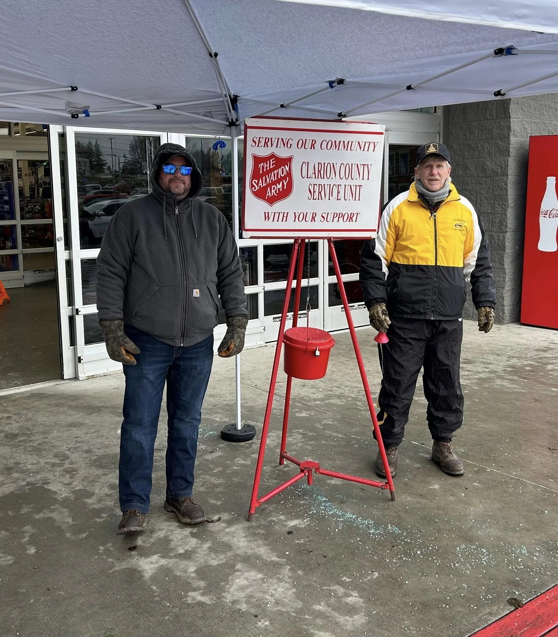 Two men standing outside a store under a tent, near a Salvation Army sign for the Clarion County Service Unit, supporting the community.
