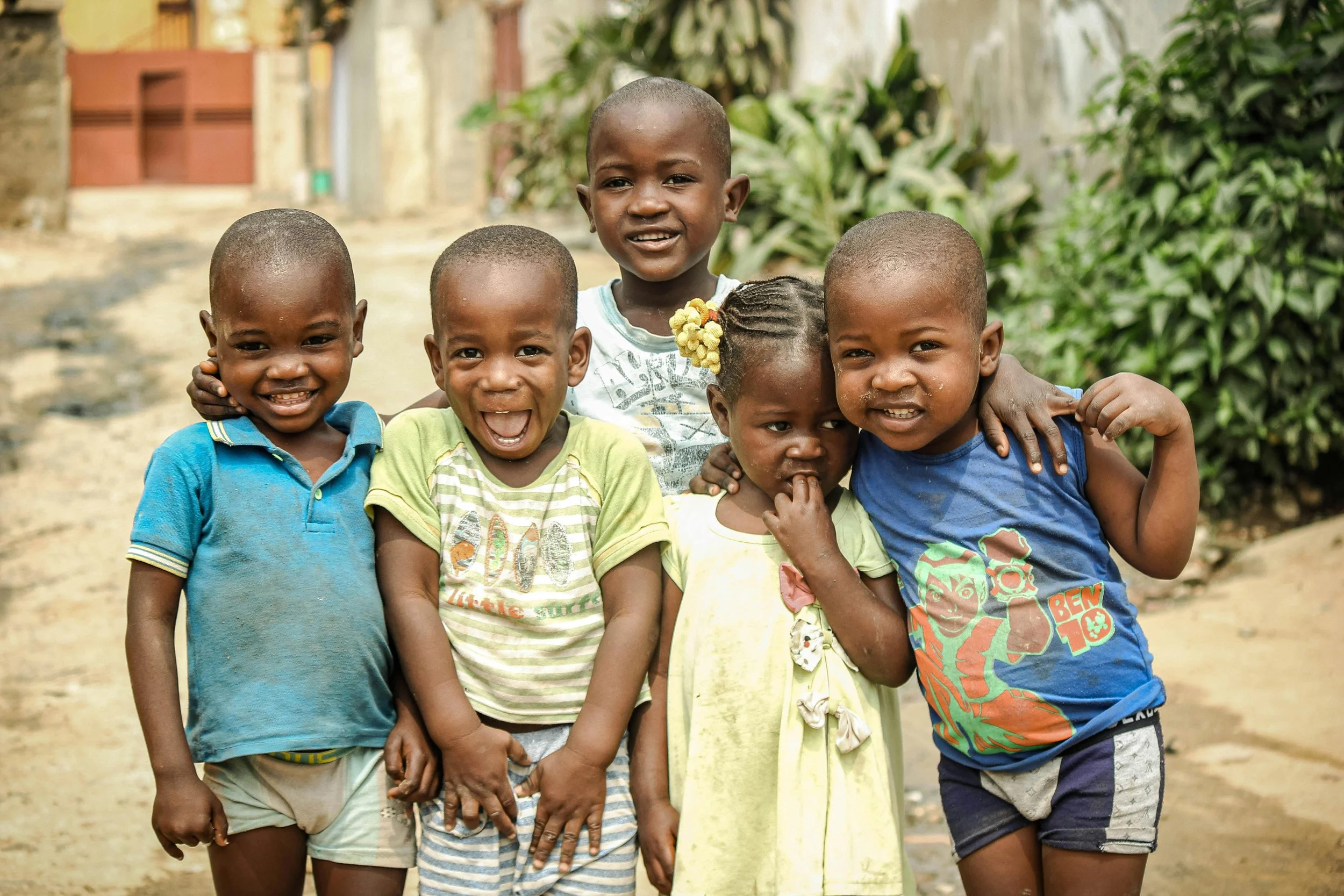 Group of six smiling and happy children standing close together outdoors.