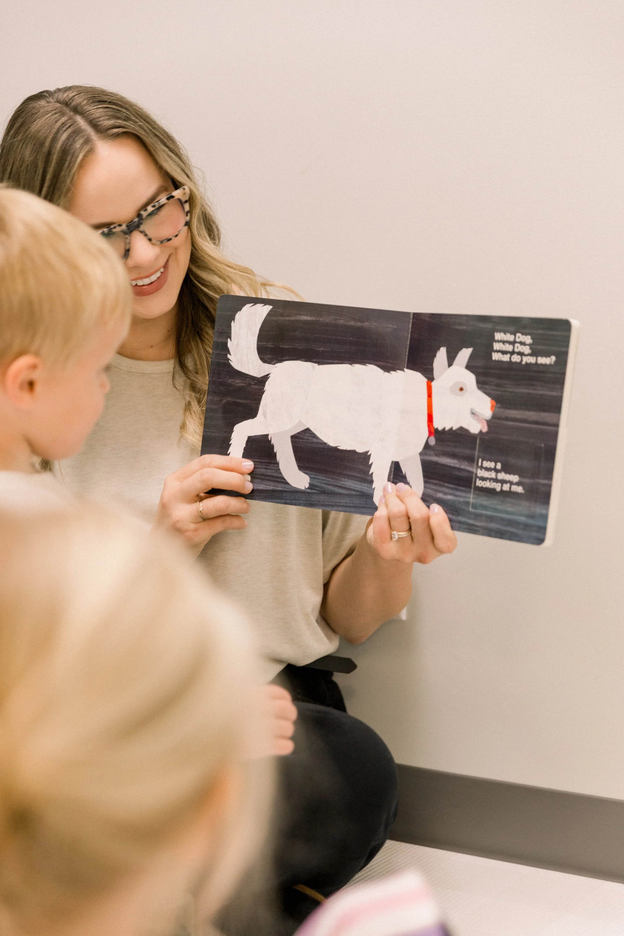 A speech therapist is reading a children's book (Brown Bear) to engaged children in a speech therapy clinic with the dog illustration on the page. Private SLP services in-clinic in Saskatoon.