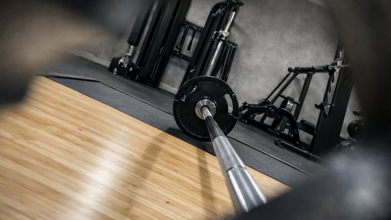 Empty gym with a barbell on the floor surrounded by other fitness equipment in the background.