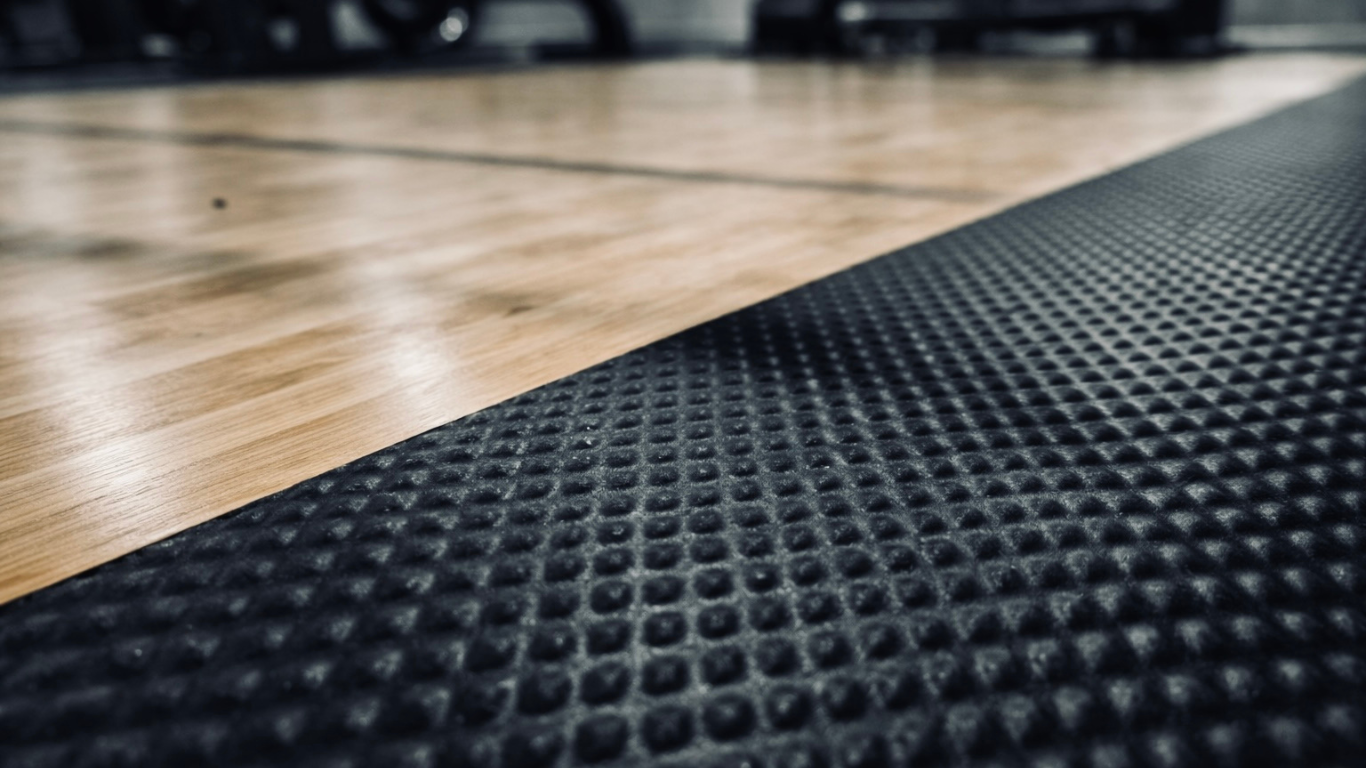 Close-up of a black textured mat on a wooden floor, possibly in a gym or workout area.
