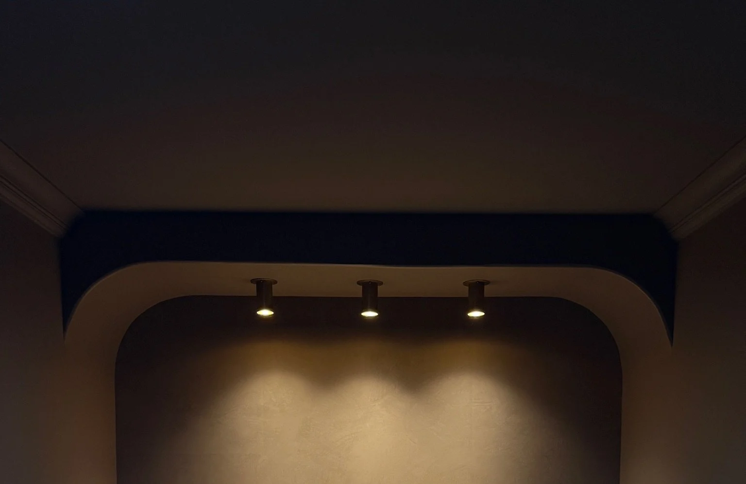 Three ceiling spotlights illuminating a textured wall in a dimly lit room.