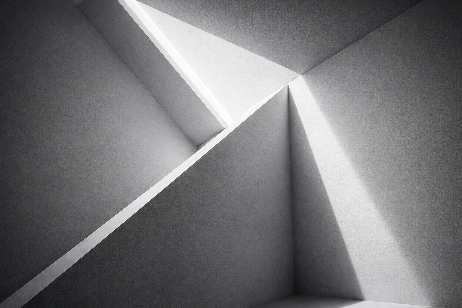 Interior view of a modern, minimalist stairwell or architectural space featuring sharp angles, natural light, and white surfaces.