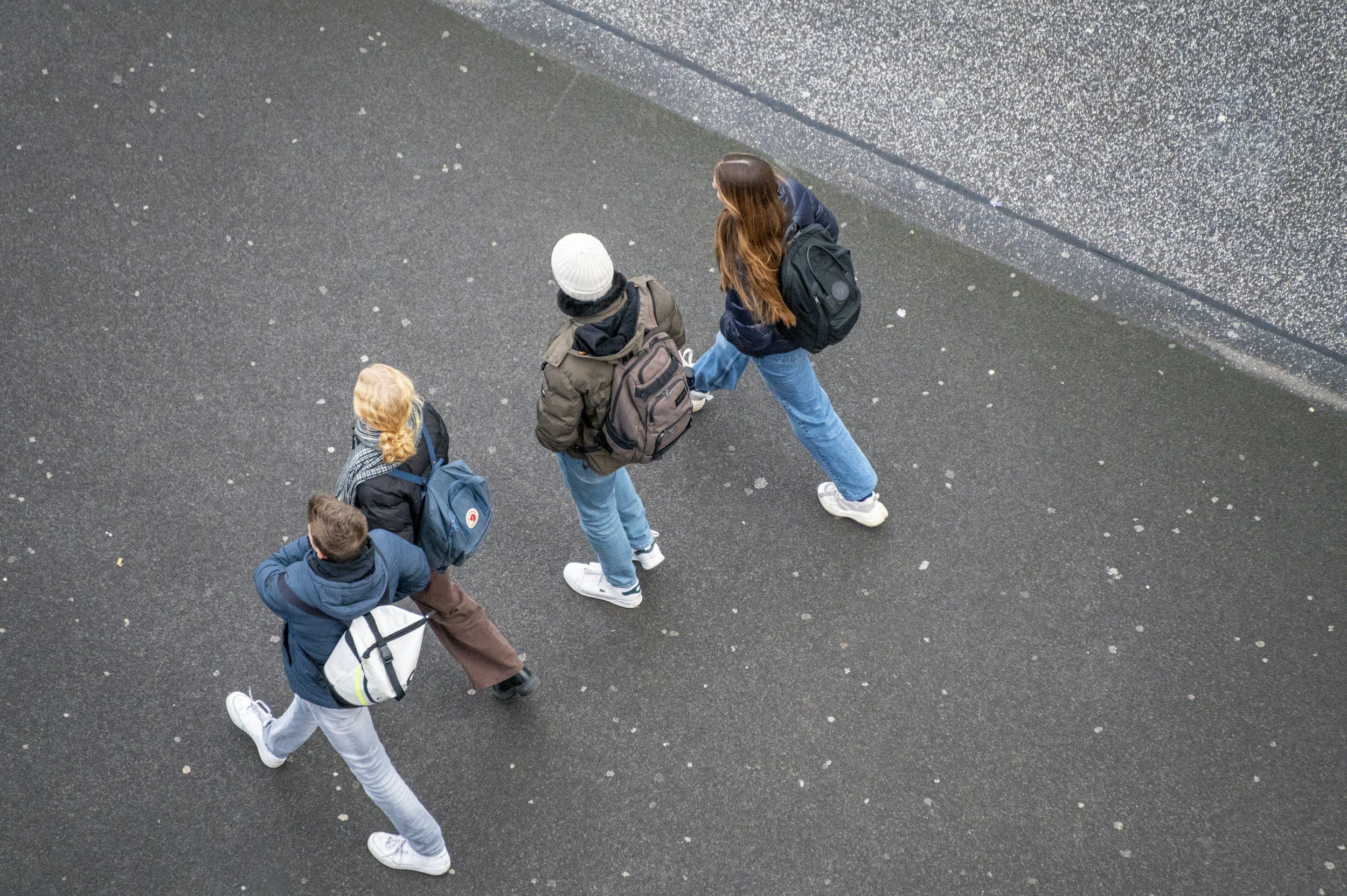Four students walking on a dark, wet outdoor pavement, carrying backpacks.