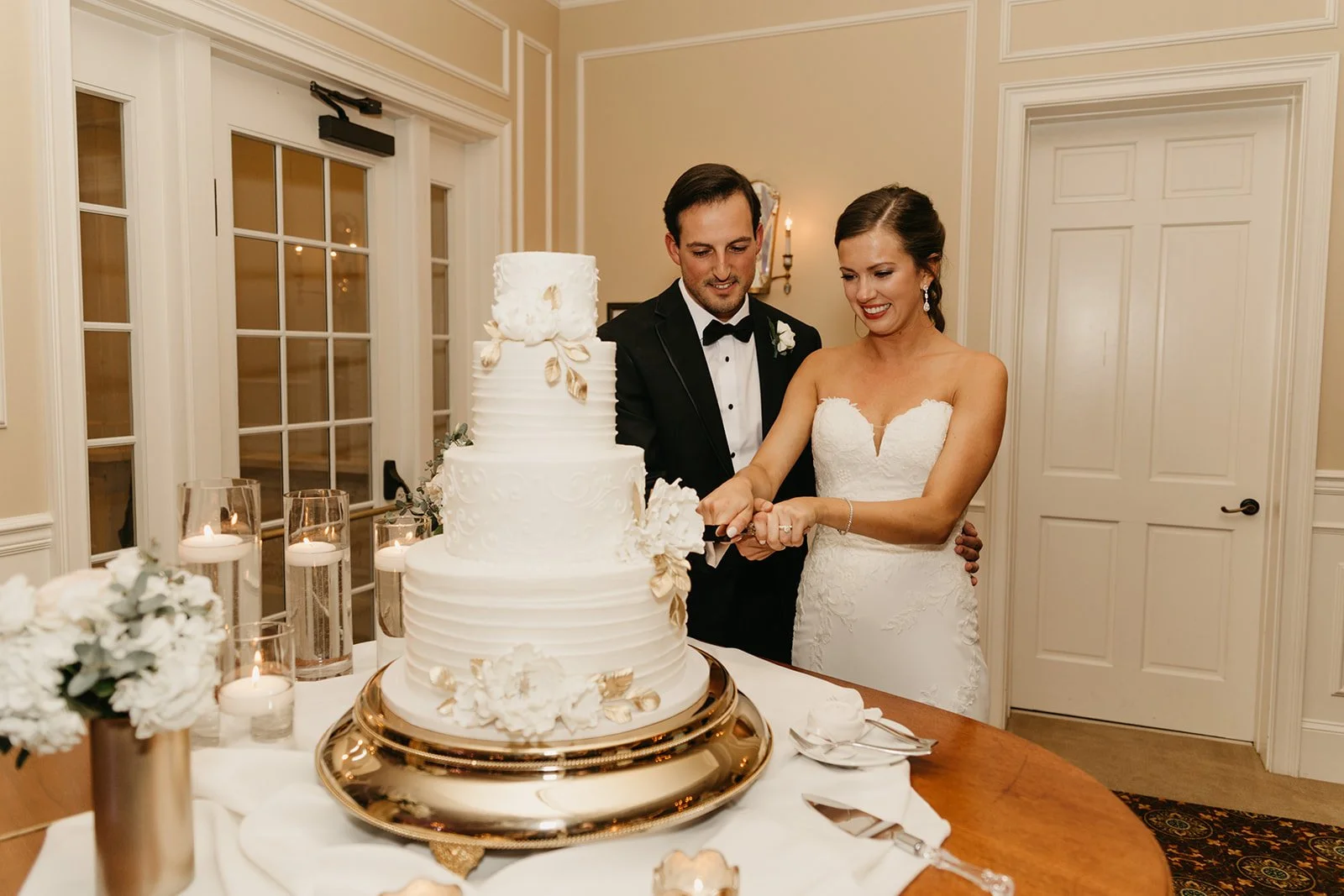 4-tier textured white buttercream cake with gold leaf and white roses at The River House by Sweet Weddings Cakes