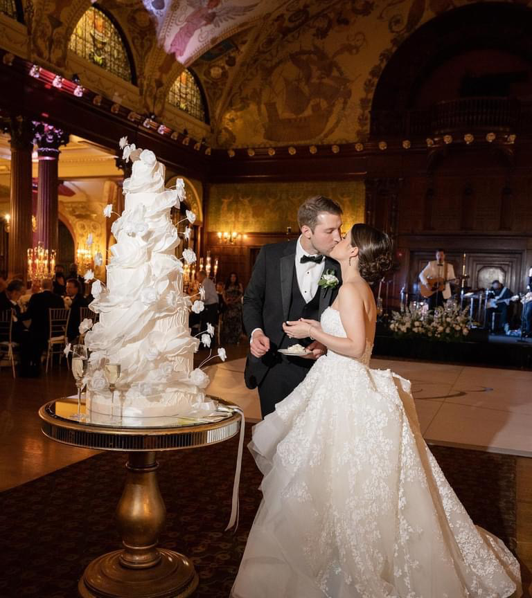 Bride and groom dancing beside an elegant five tier wedding cake at a luxury wedding reception.