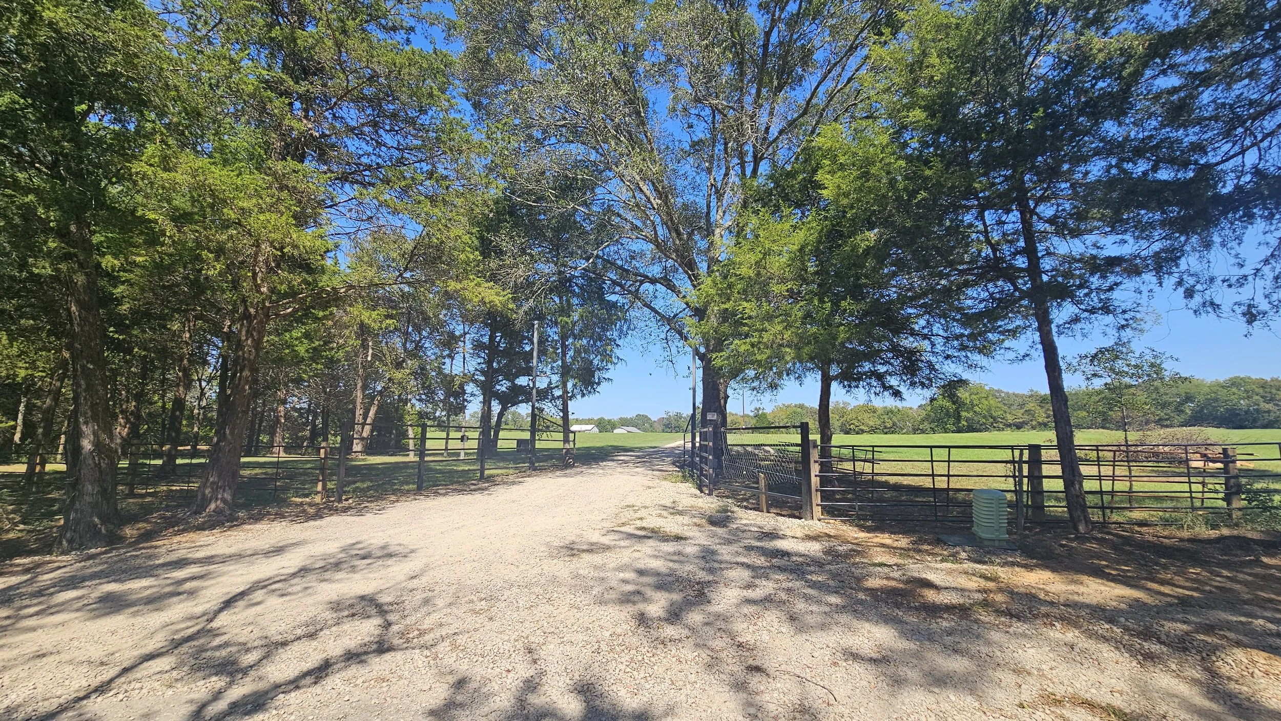 Gravel entrance road leading through a black metal gate into the wooded 465-acre Pinoy Ranch retreat in Canton, TX.