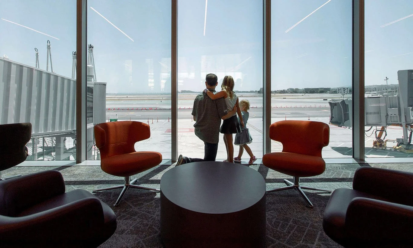 Family of four at an airport terminal, looking out the window at the tarmac and runway.