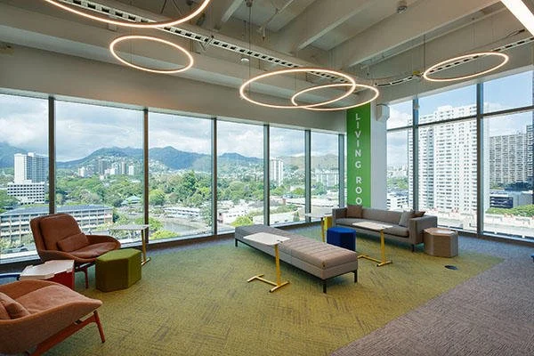 Modern lounge area with large windows showing city and mountains, circular ceiling lights, chairs, sofas, and a green banner with 'LIVING ROOM' in white text.