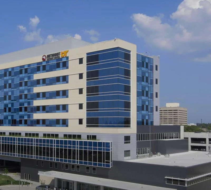 Modern multi-story office building with blue-tinted glass windows and a Yale New Haven logo at the top, under a partly cloudy sky.