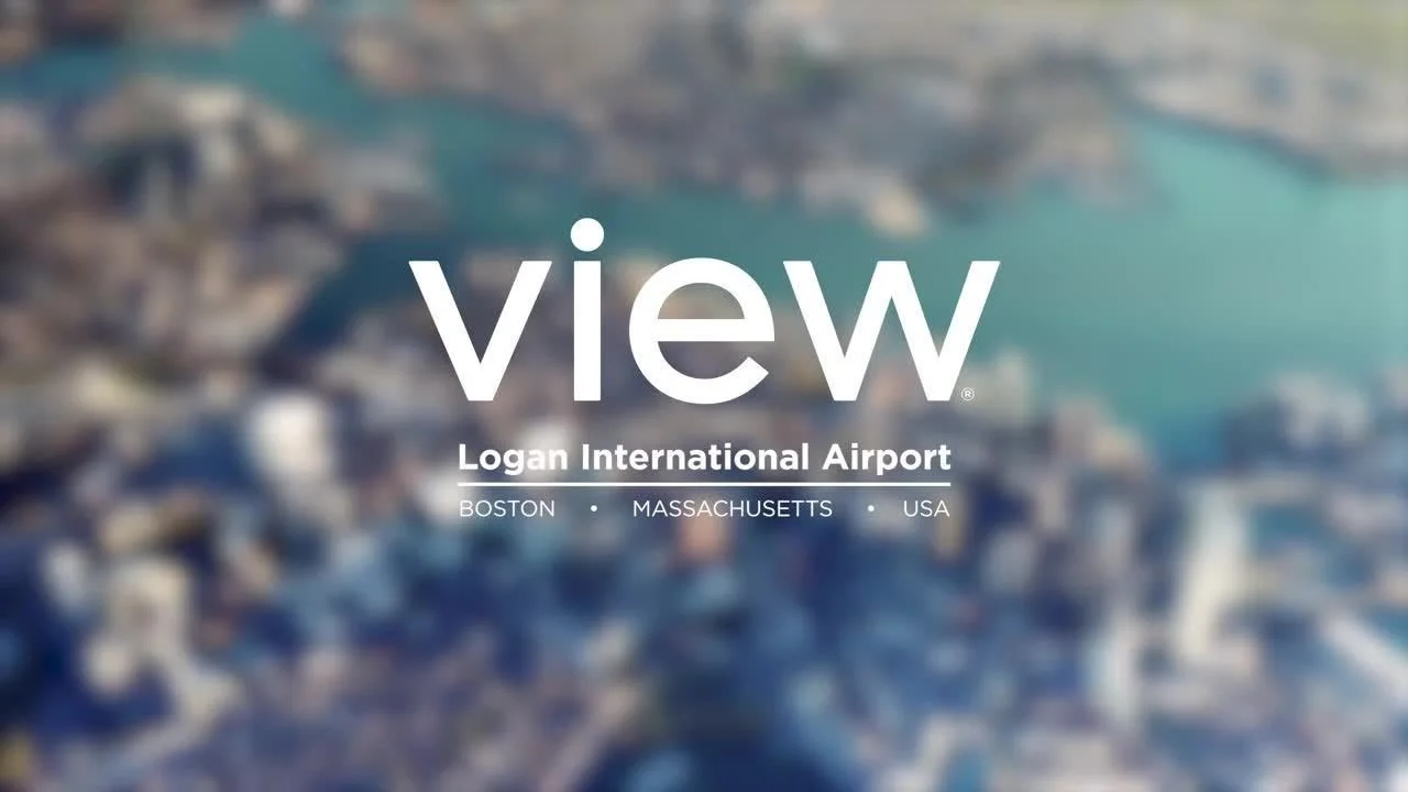 Aerial view of Boston cityscape with harbor area, featuring buildings, water, and bridges, with overlaid text 'view,' 'Logan International Airport,' and location details.