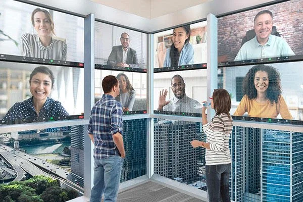 Three people in a conference room with multiple video call screens showing eight individuals participating in a virtual meeting, with city buildings visible outside.