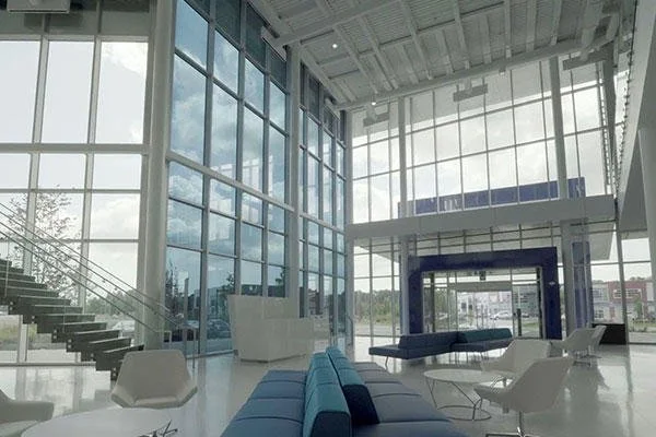 Interior view of a modern, spacious building with large glass windows, white walls, and contemporary furniture including blue and white seating areas.