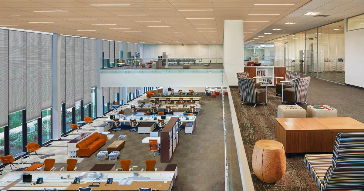 Modern office space with open floor plan, workstations, and a mezzanine lounge area with chairs and bookshelves.
