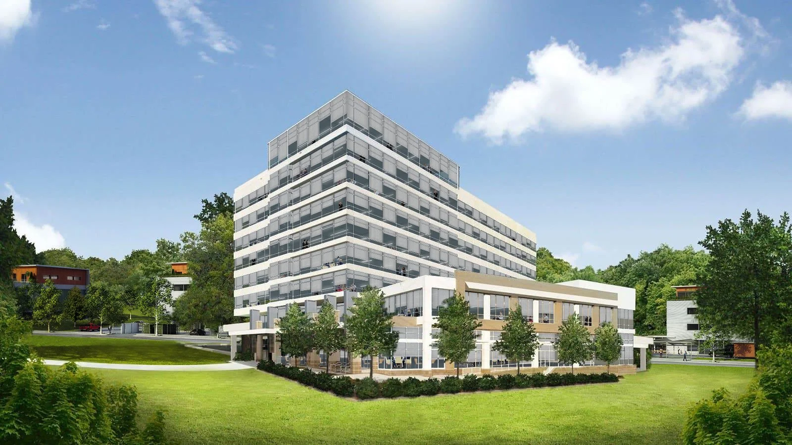 Modern multi-story office building with many glass windows, surrounded by green grass, trees, and a blue sky with clouds.