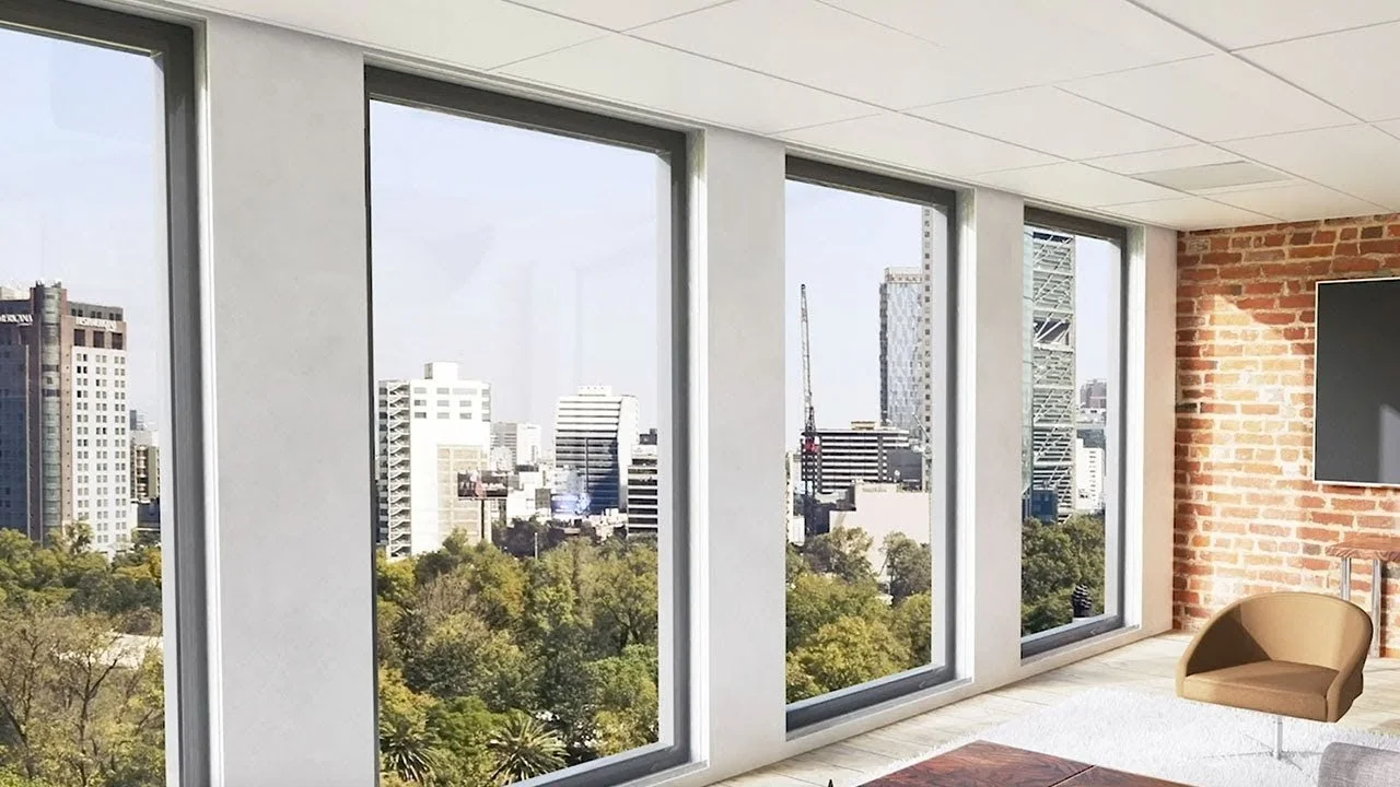A modern apartment living room with large floor-to-ceiling windows showing a city skyline and green trees outside.