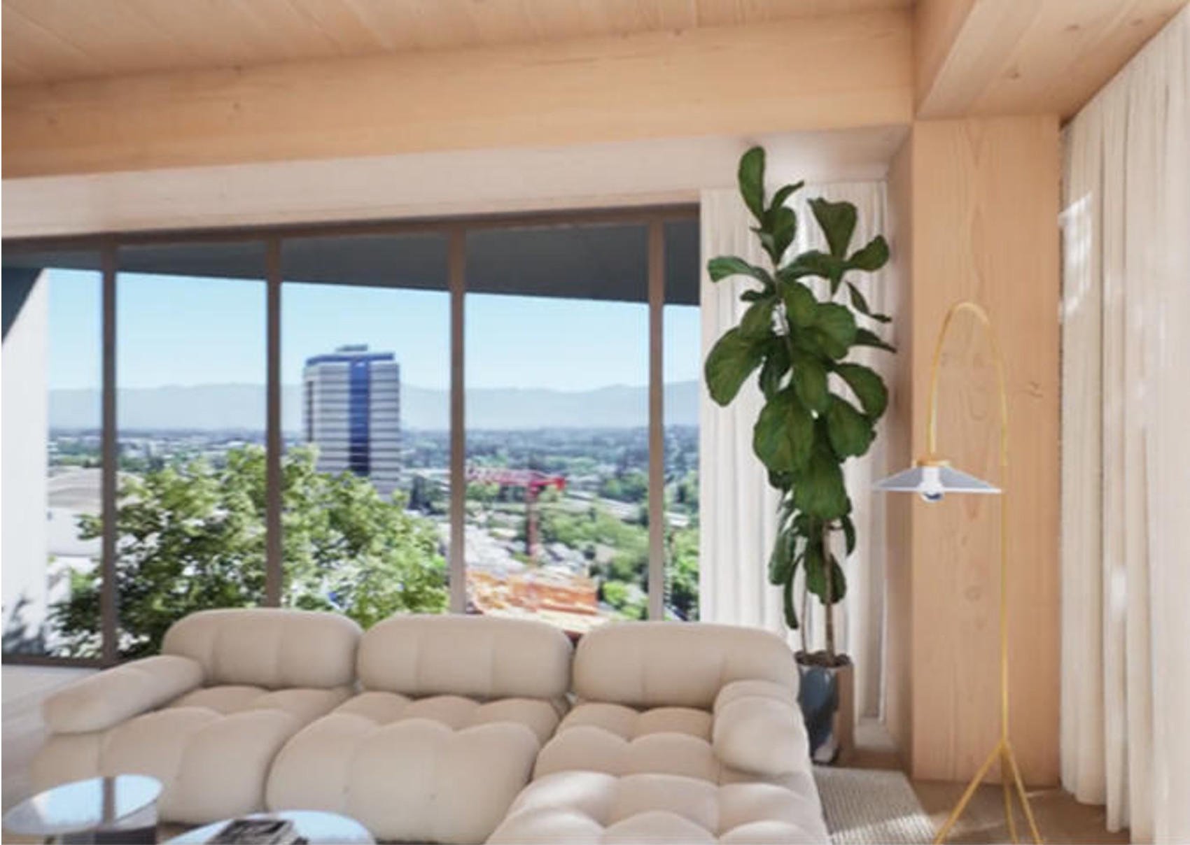 Living room with large window overlooking cityscape and greenery, beige sectional sofa, tall potted plant, wooden wall, and standing lamp with yellow stand.
