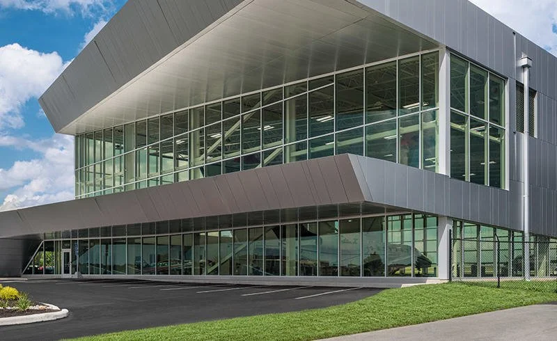 Modern two-story office building with glass exterior windows and a parking lot in front.