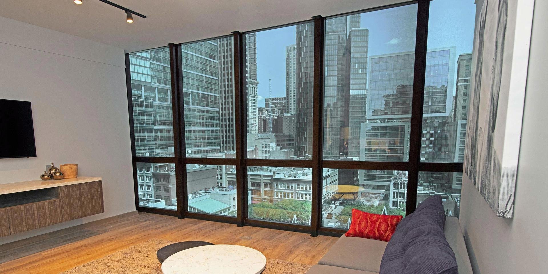 Modern living room with large floor-to-ceiling windows overlooking a city skyline, featuring high-rise buildings and skyscrapers.