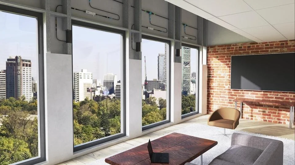 Modern office with large windows overlooking a city skyline, brick accent wall, flat screen TV, brown armchair, gray sofa, wooden table, and a laptop.