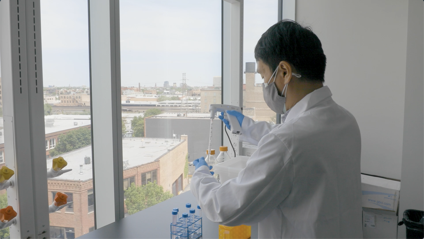 A scientist wearing a mask, gloves, and a lab coat performing an experiment with test tubes near a large window overlooking a cityscape.