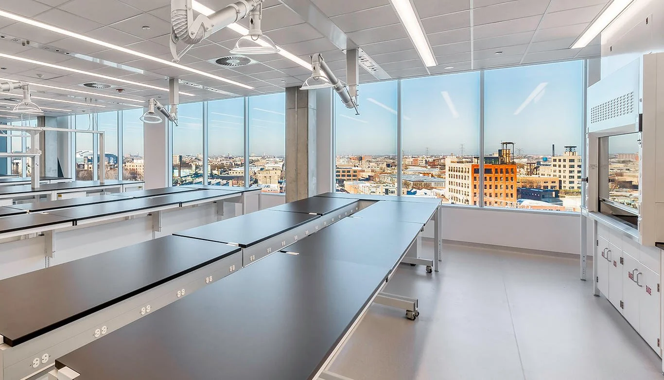 Empty science classroom with lab tables, large windows showing cityscape, and scientific equipment.