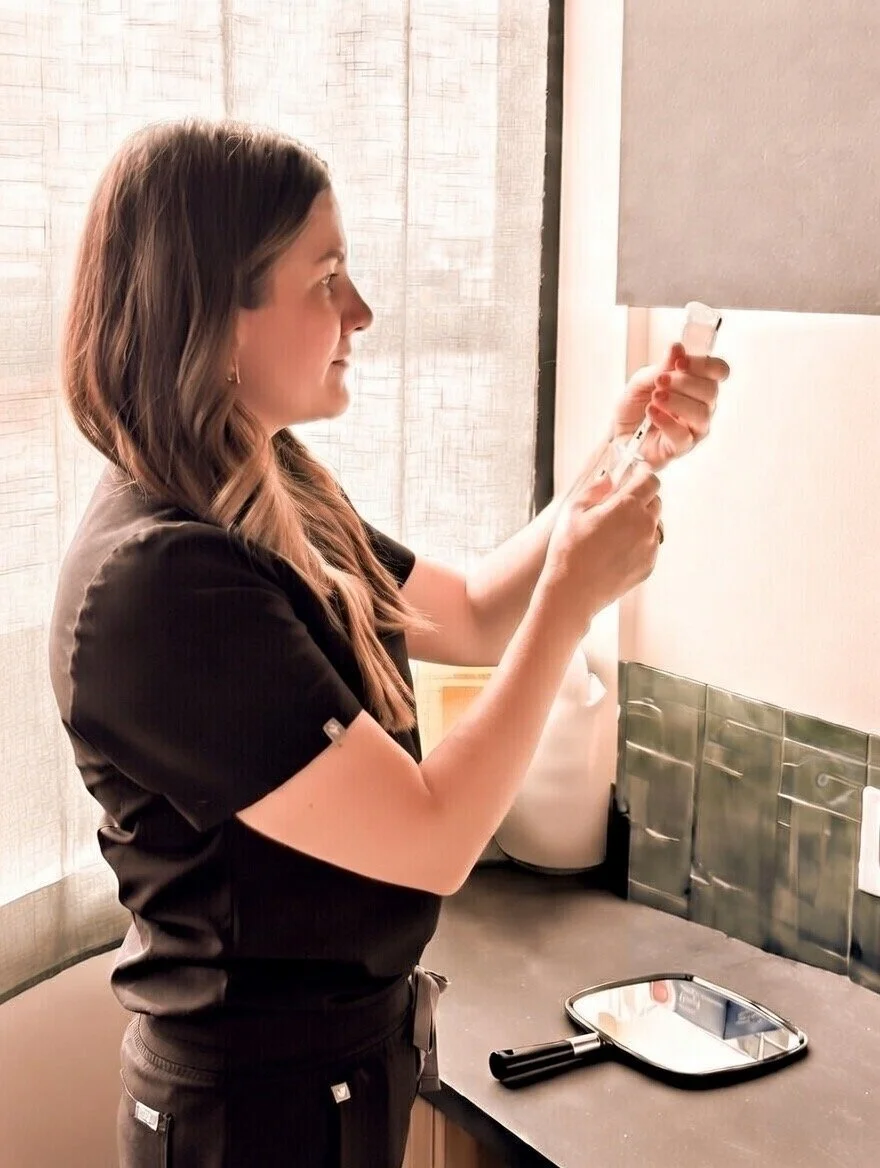 A woman in black scrubs preparing a syringe at a hospital or clinic setting.