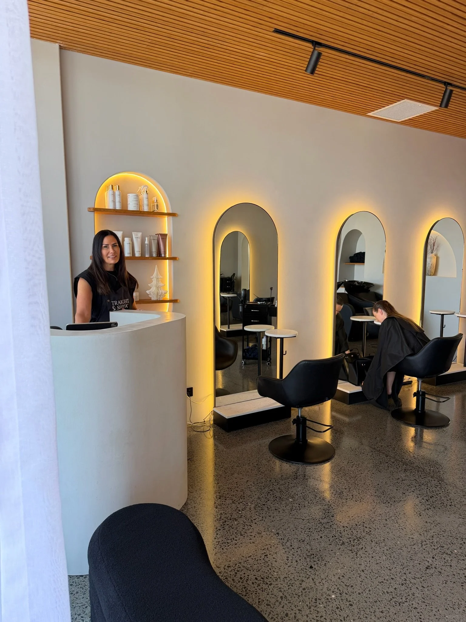 Founder of Straight & Sleek hair straightening salon standing at the reception desk inside the Kirra studio.