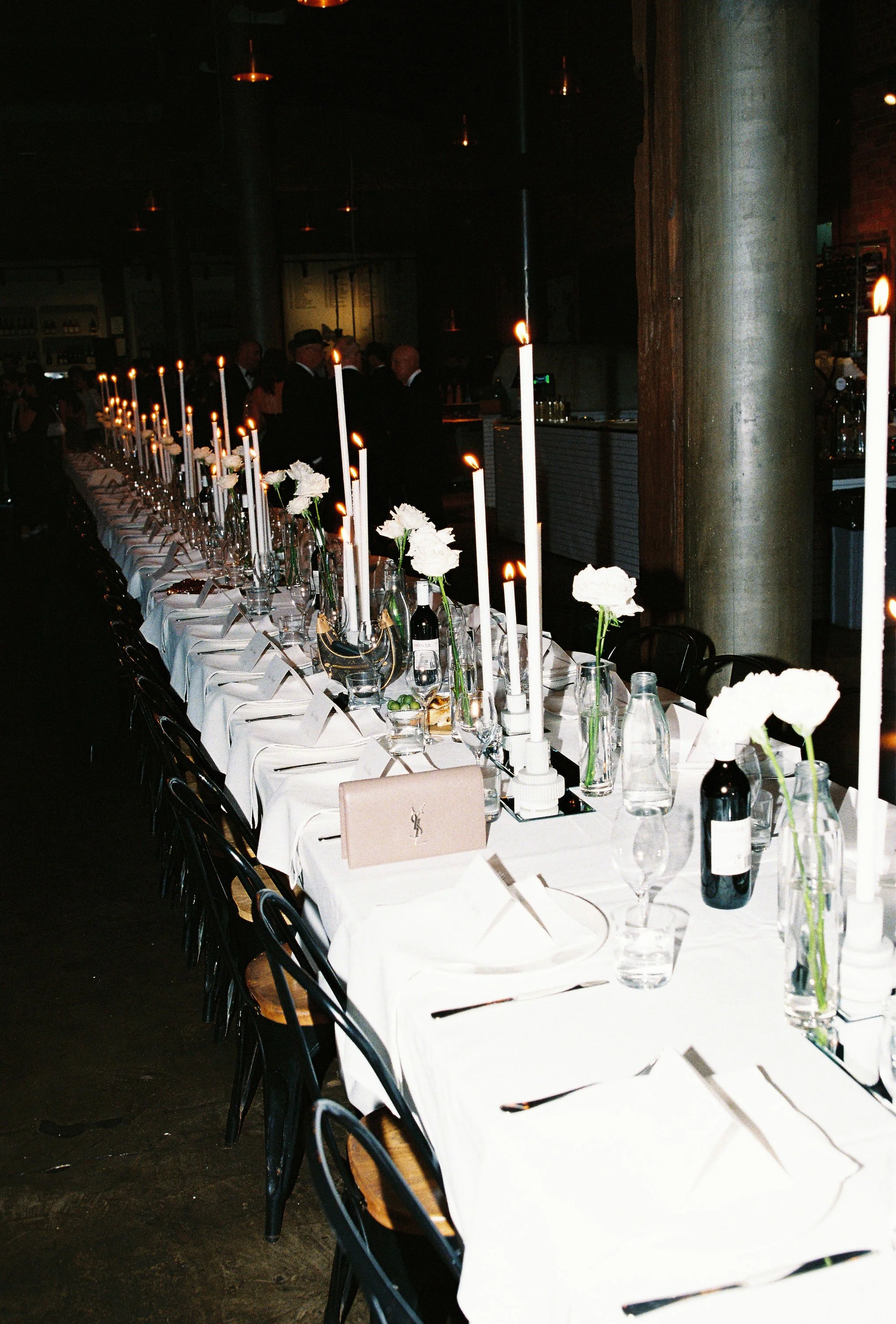Long dining table with white tablecloth, set for a wedding at The Epicurean Red Hill with white flowers, tall white candles, wine glasses, all coordinated by Alex Morabito for Ever After Effect.