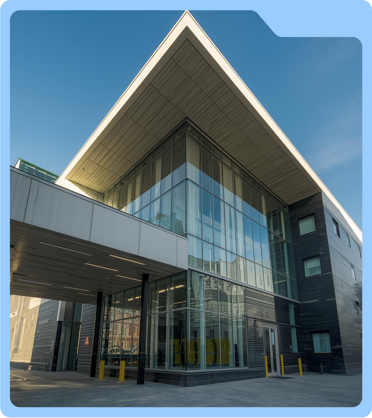 Modern office building with glass walls and overhanging roof, yellow bollards in front, sunny day with blue sky.