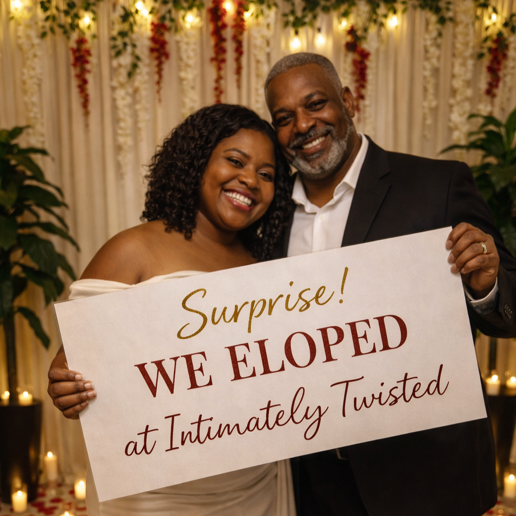 A smiling couple holding a sign that says, "Surprise! We eloped at Intimately Twisted," at a decorated indoor wedding venue.