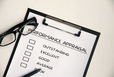 Performance appraisal form on clipboard with checkboxes for rating options and a pen, pair of glasses nearby.