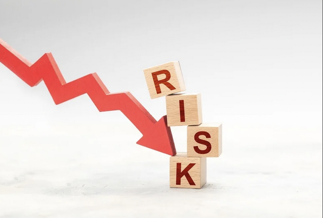 Wooden blocks spelling 'RISK' stacked under a downward red arrow, indicating decreasing risk or financial decline.