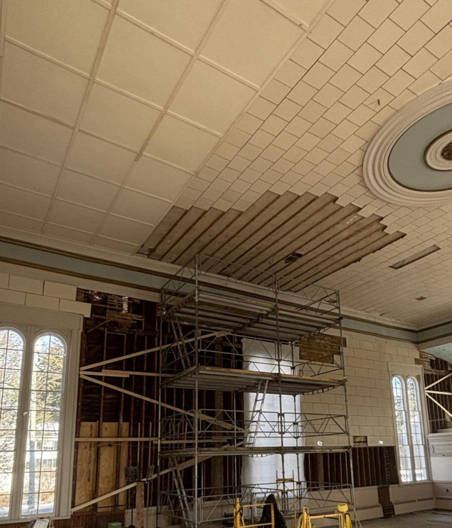 Construction scaffolding inside the main hall with a decorative ceiling, large windows, and partially installed ceiling panels or tiles.