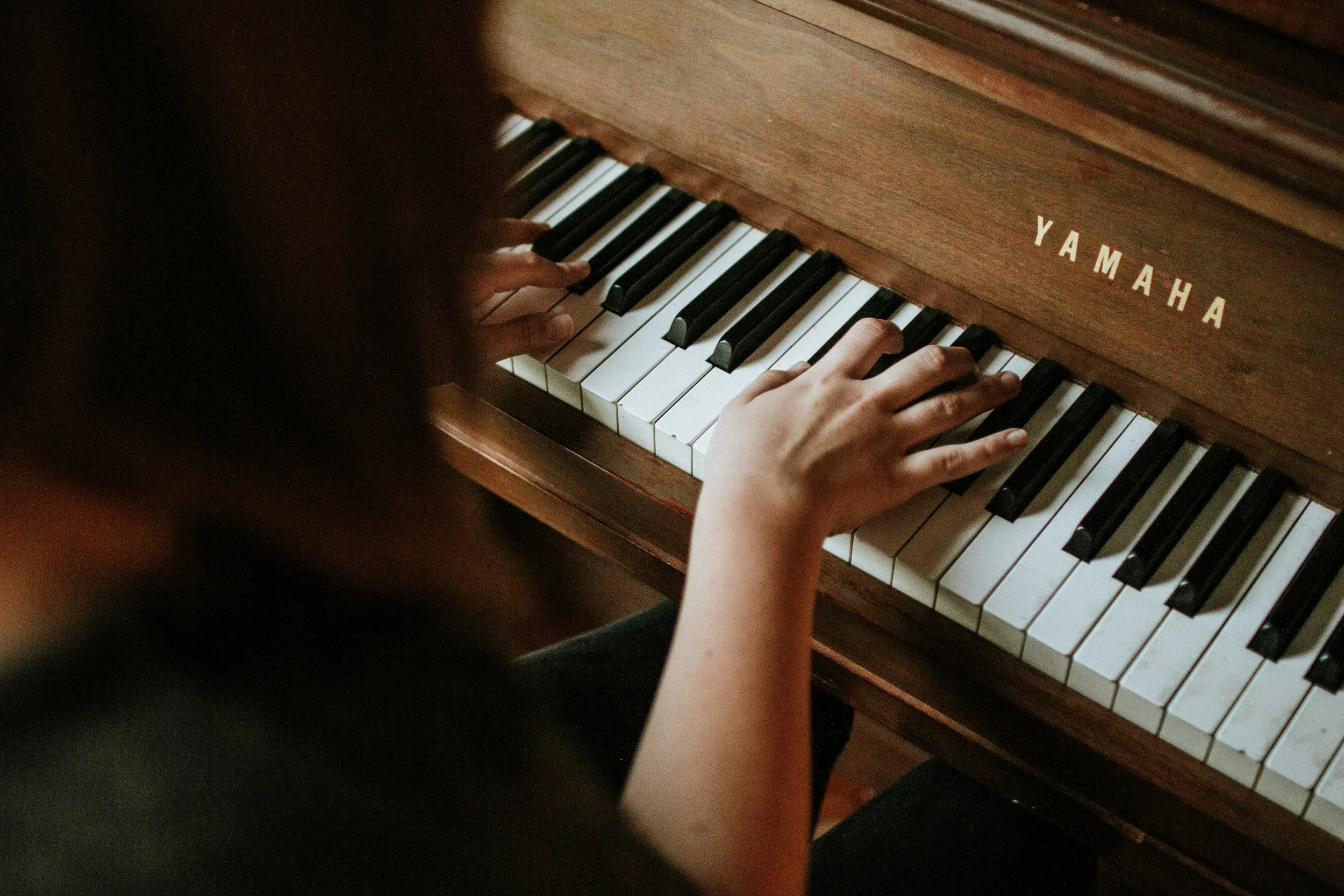 Child playing piano, focusing on hands on black and white keys, Yamaha brand visible on wooden piano.