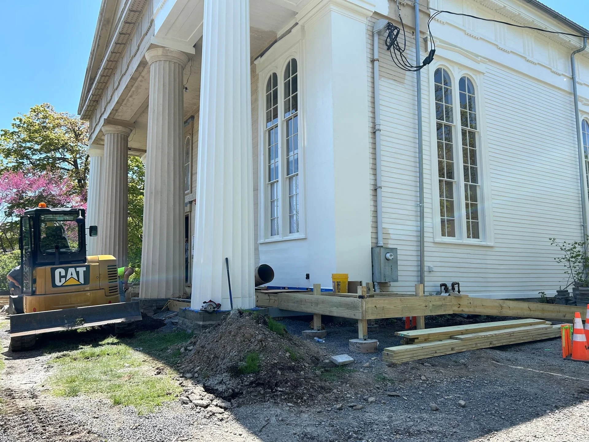 Construction workers working on the front porch of TCFA with tall columns, construction materials, and equipment nearby.