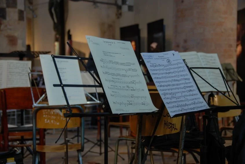 Music stands with sheet music in a dimly lit room, likely a venue for a live musical performance.